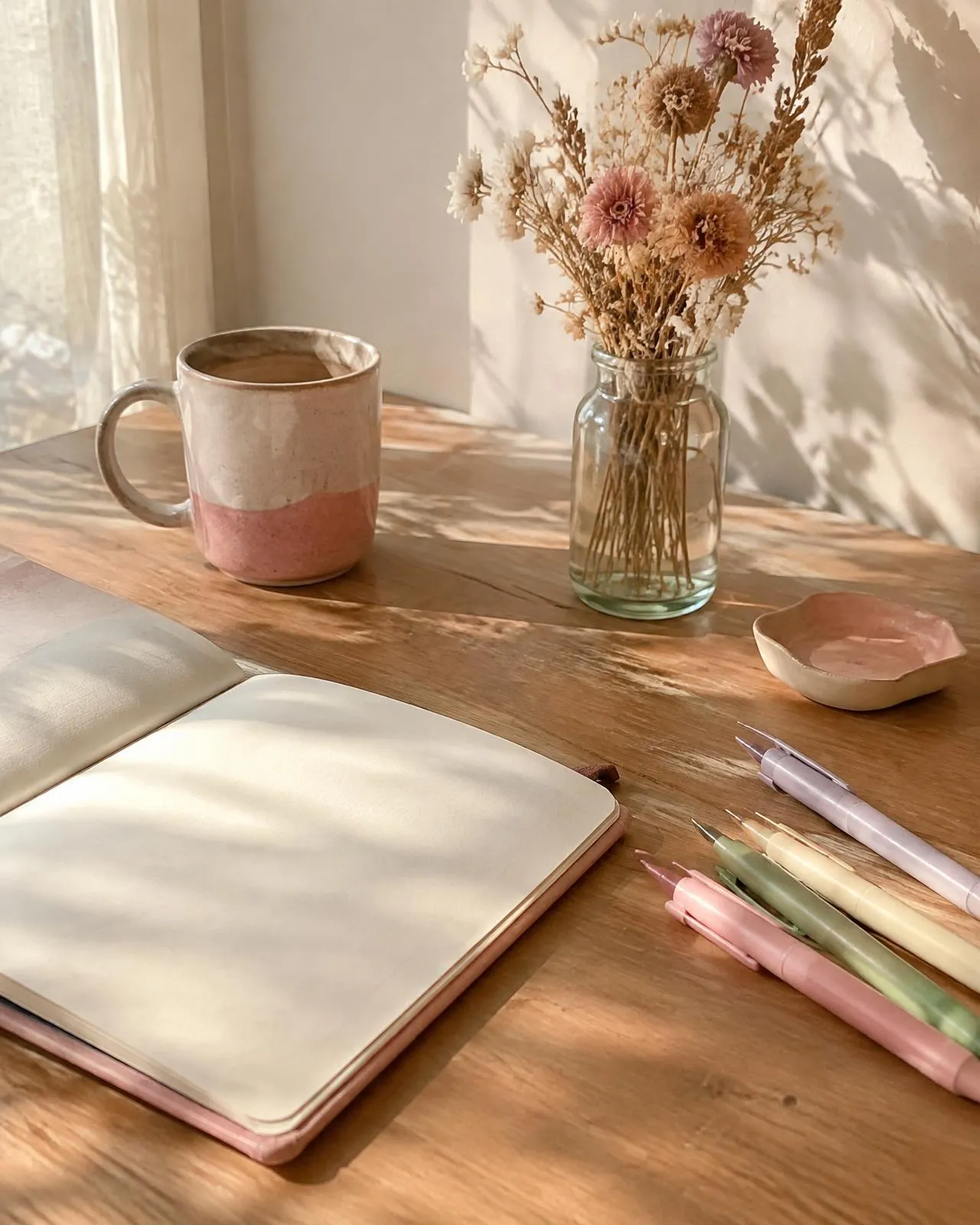 Journal, colored pens and a mug on a sunlit desk